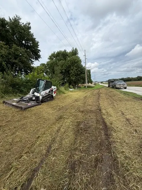Skid steer on a freshly mown roadside ditch