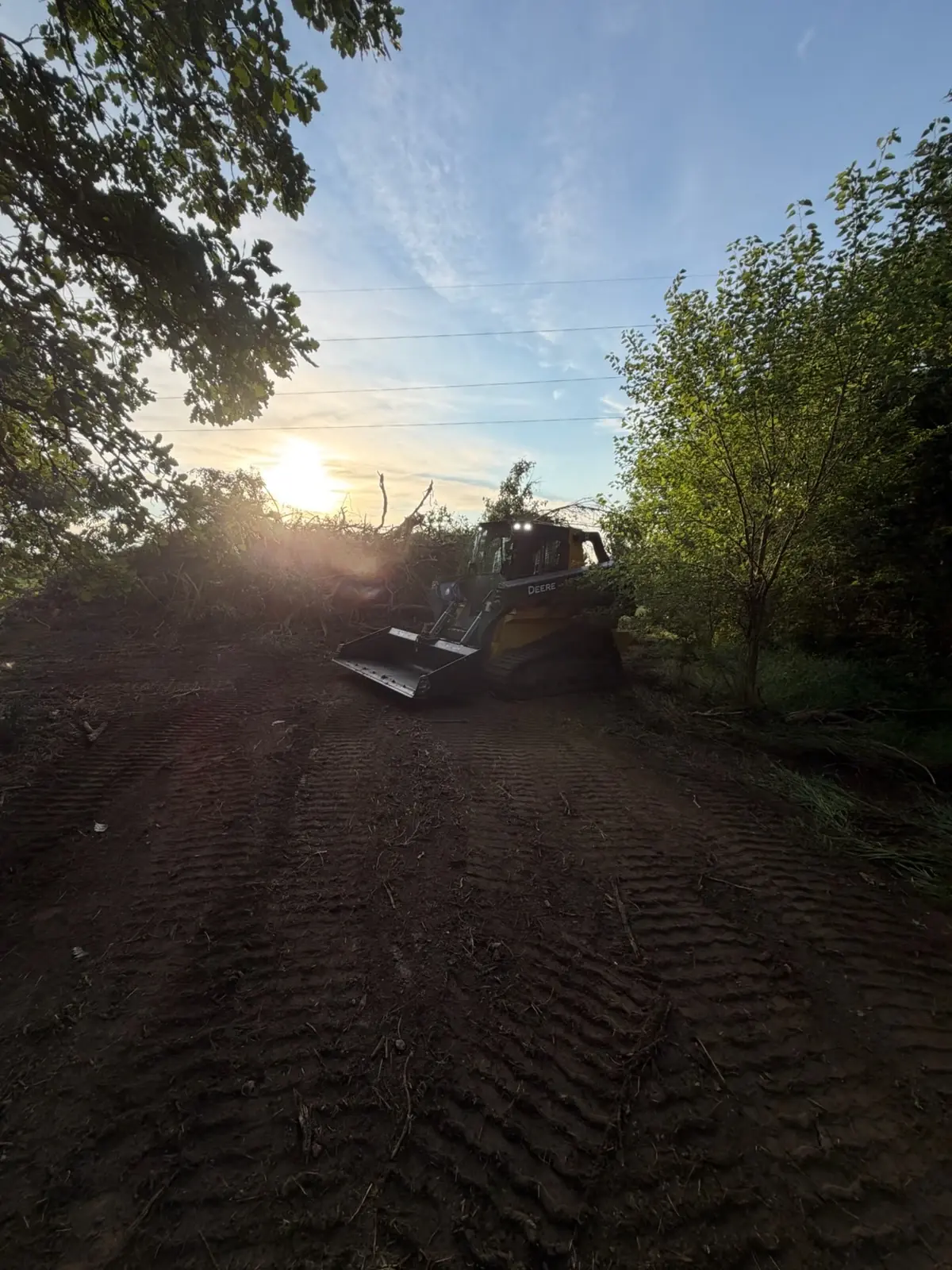 John Deere skid steer preparing cleared ground at sunset